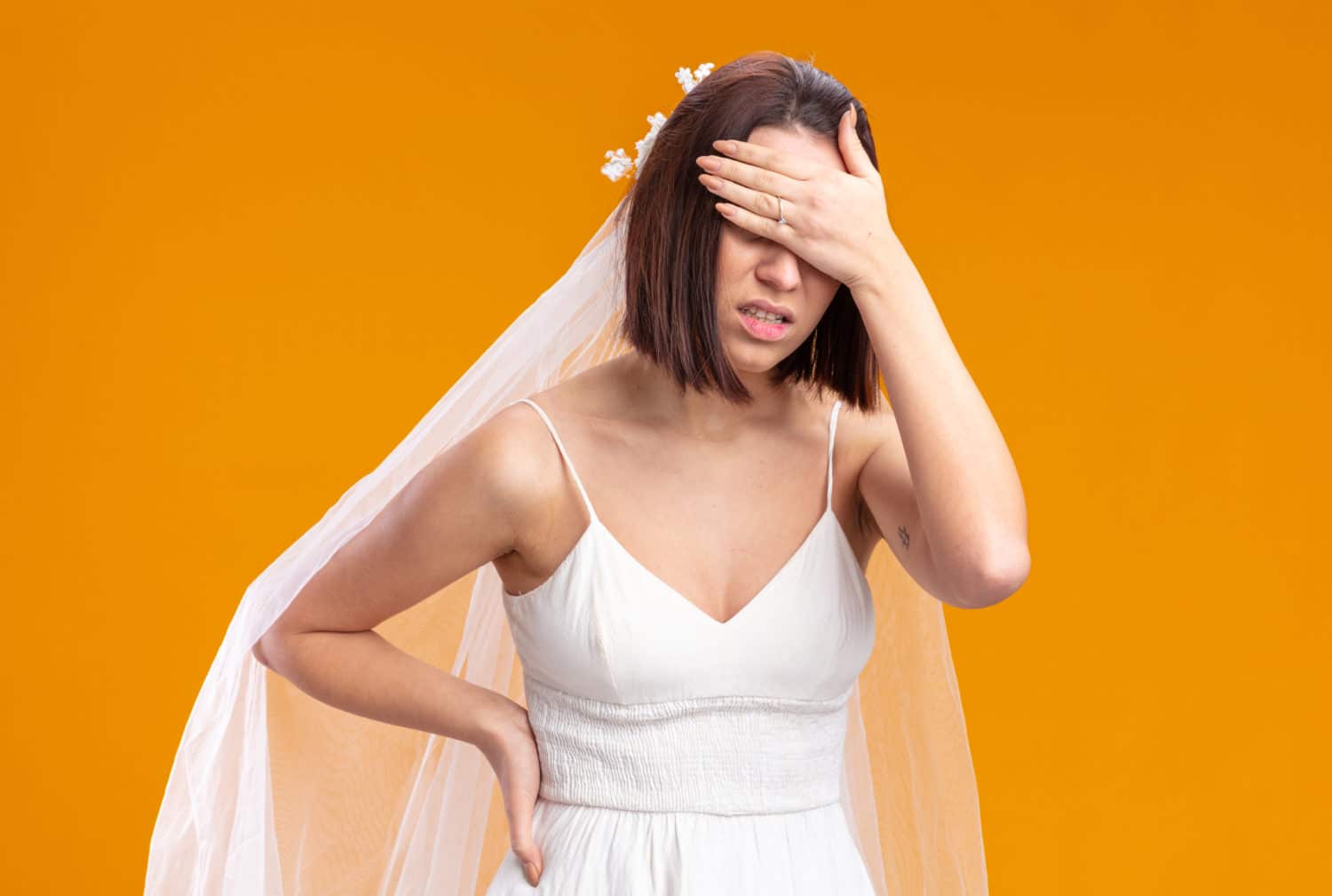 braut im schonen hochzeitskleid das unwohl aussieht und die augen mit der hand bedeckt die uber der orangefarbenen wand steht